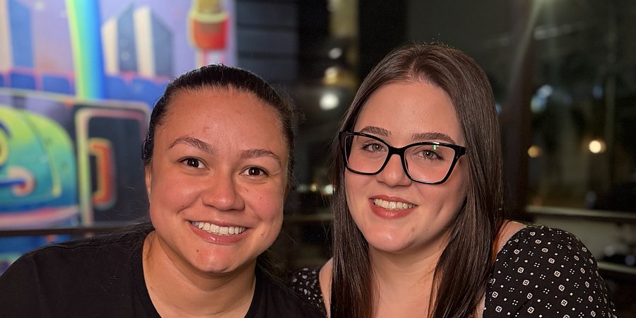 Emilliani e Lauanny, criadoras do Rolezando, sorrindo à mesa em um restaurante à noite